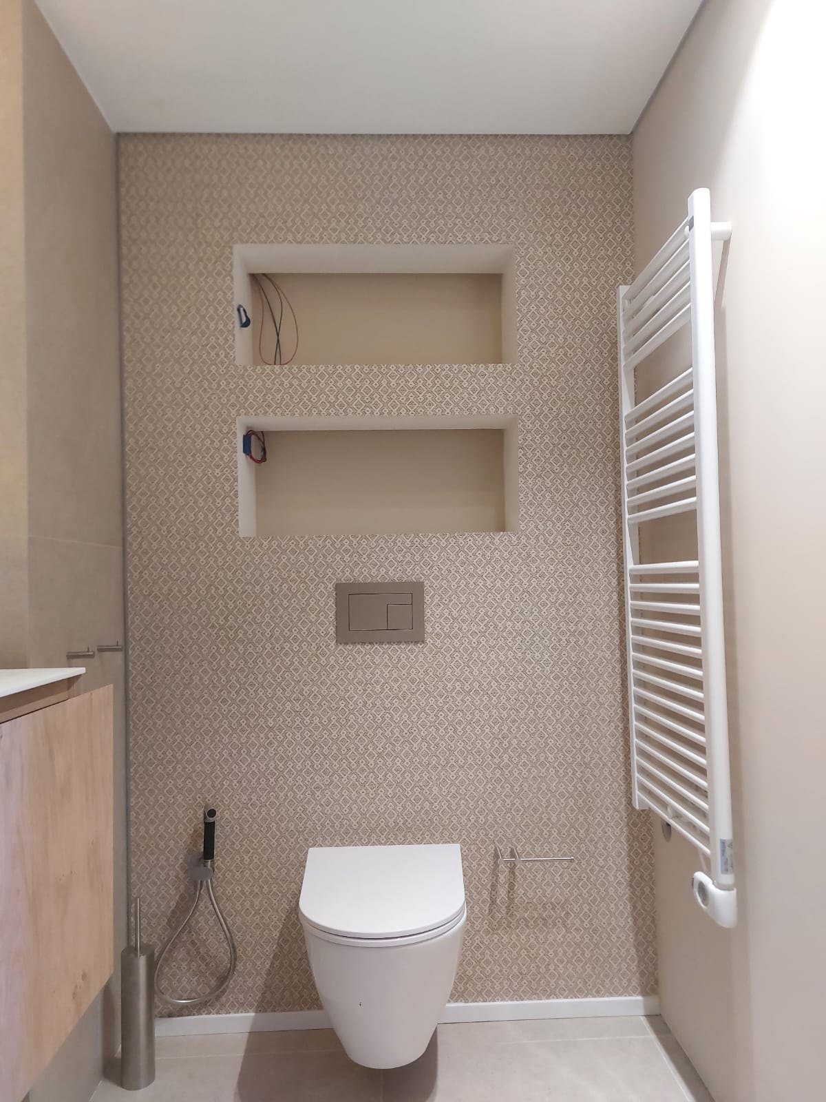 Baño reformado con papel pintado beige texturado y hornacinas de obra