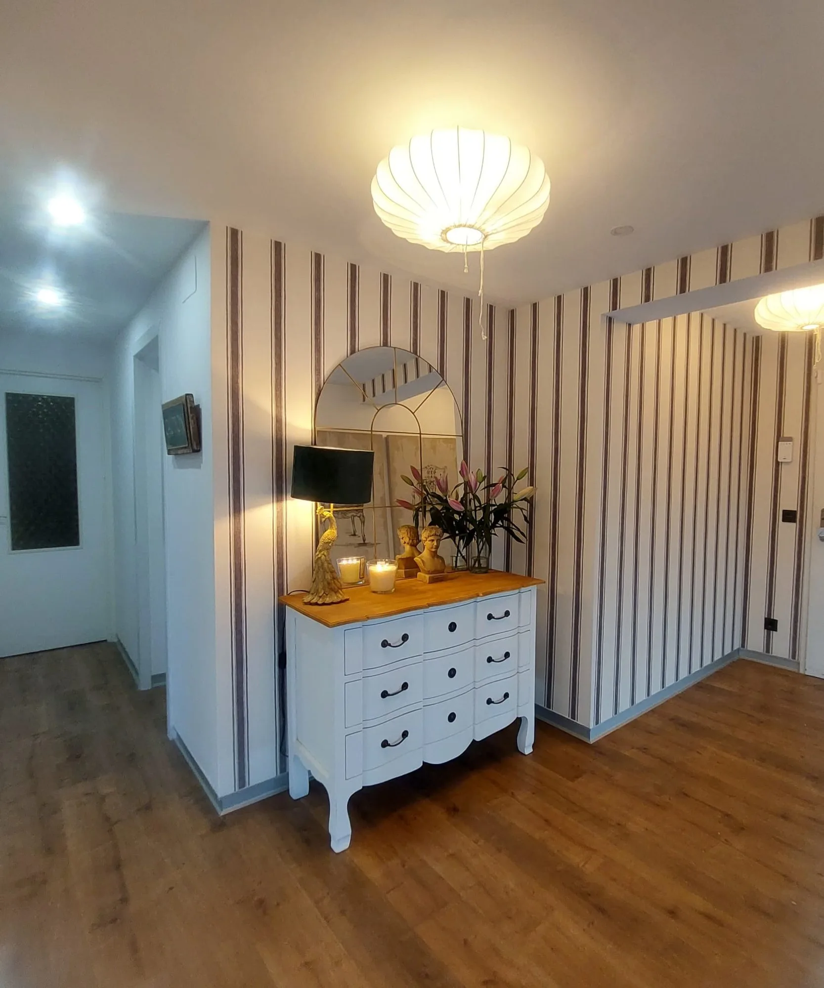 Recibidor con papel pintado de rayas verticales en tonos madera junto a una cómoda blanca