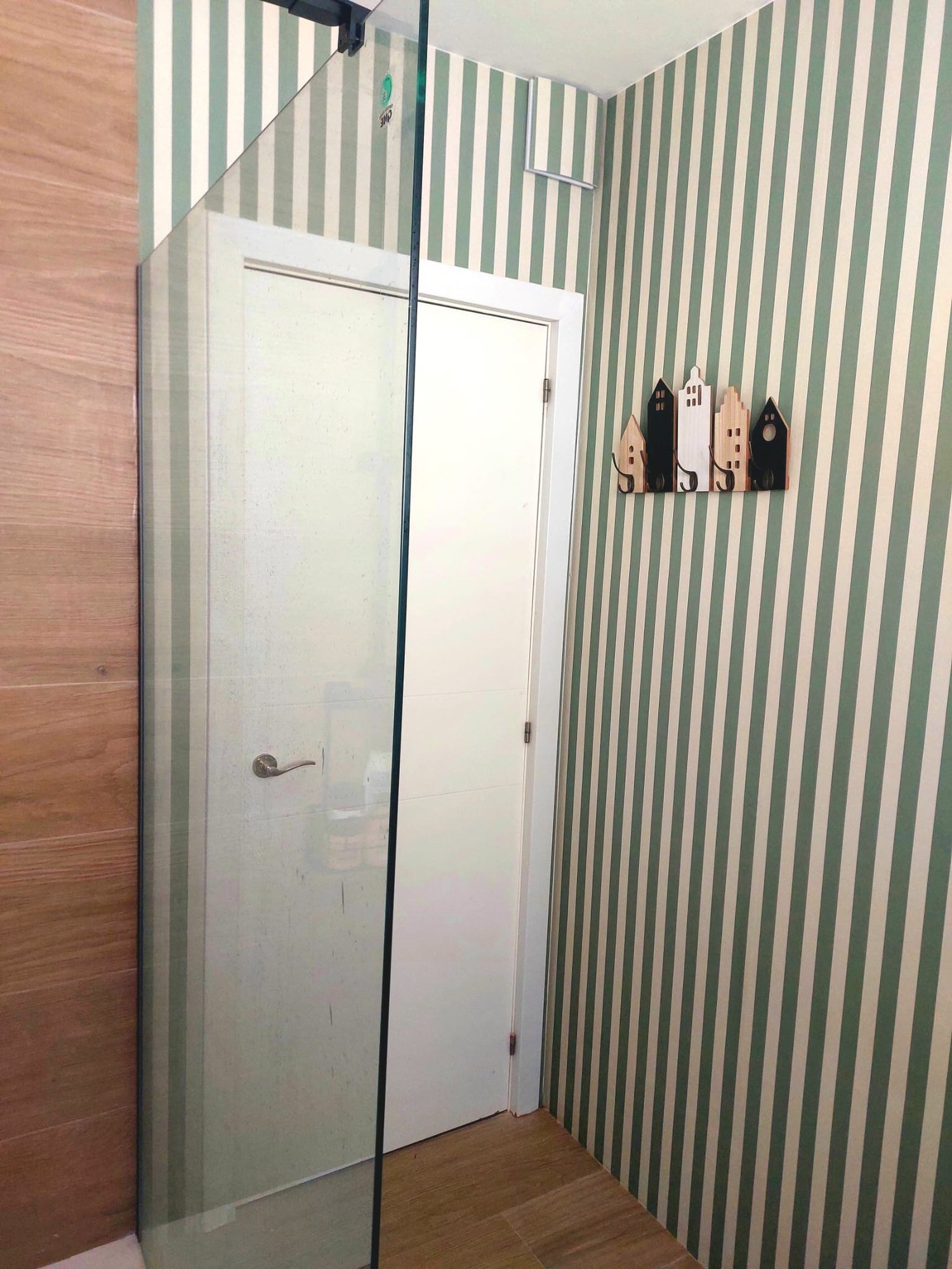 Baño con papel pintado de rayas verdes junto a una mampara de ducha