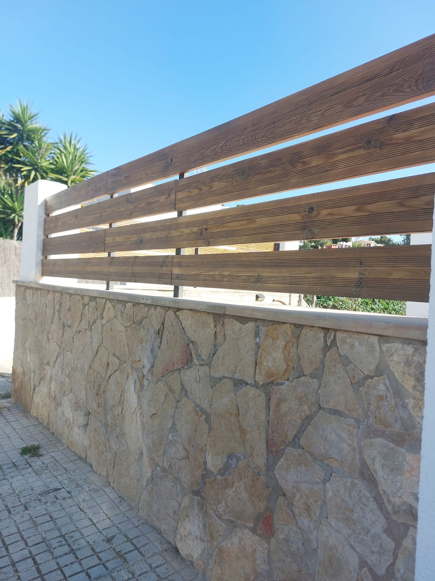 Valla de madera tratada instalada sobre un muro de piedra en el exterior de una vivienda